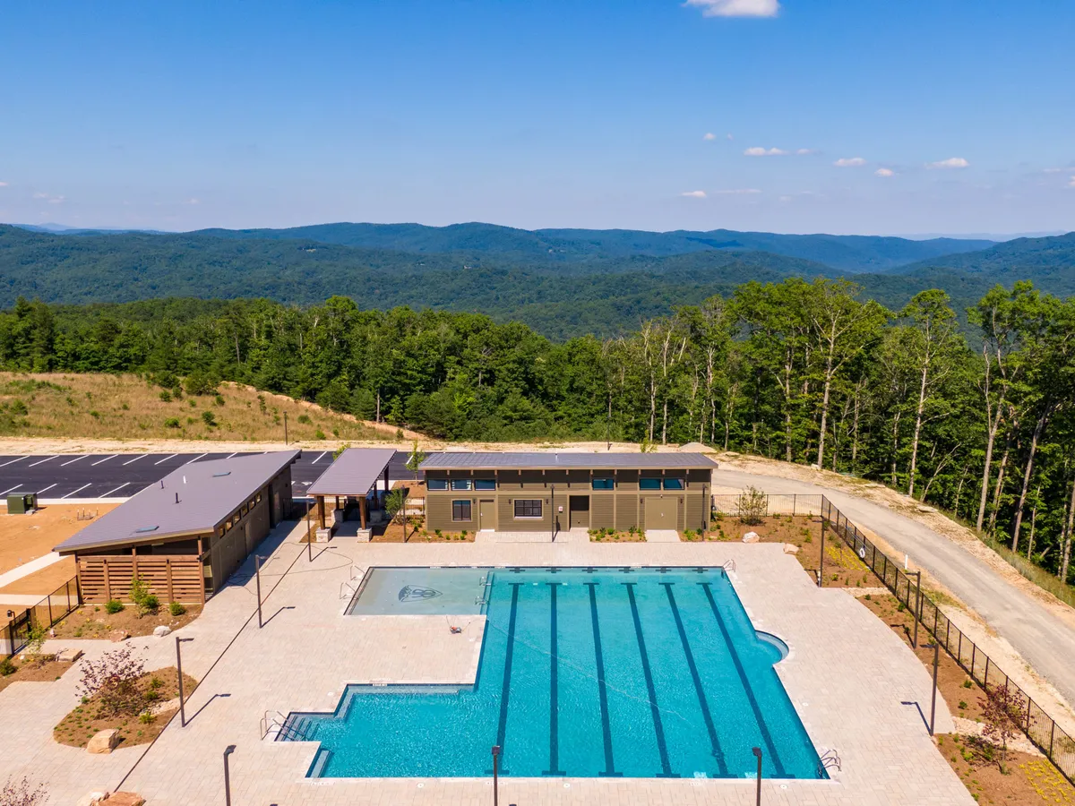 A sparkling swimming pool is nestled amidst the mountains, with a surrounding recreation area and adjacent building structure. The pool area is lively yet peaceful, hinting at both relaxation and social opportunities for all ages. Mountain views in the background reinforce the unique setting.