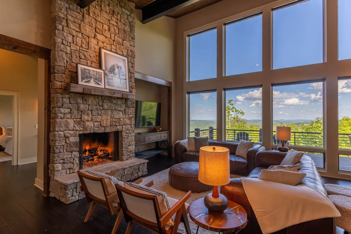 This living space is centered around a stone fireplace, surrounded by comfortable seating and large windows that offer breathtaking mountain views. Artwork and decorative touches add a personal, welcoming feel.