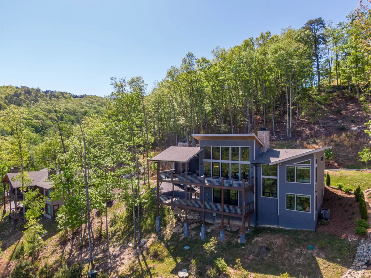 This scene captures the modern exterior of the property, focusing on its expansive deck area framed by large windows and surrounded by trees. The deck is designed for gatherings, relaxation, and scenic enjoyment, with nature trails nearby inviting exploration. The tranquil setting and architectural details emphasize both comfort and access to the outdoors.