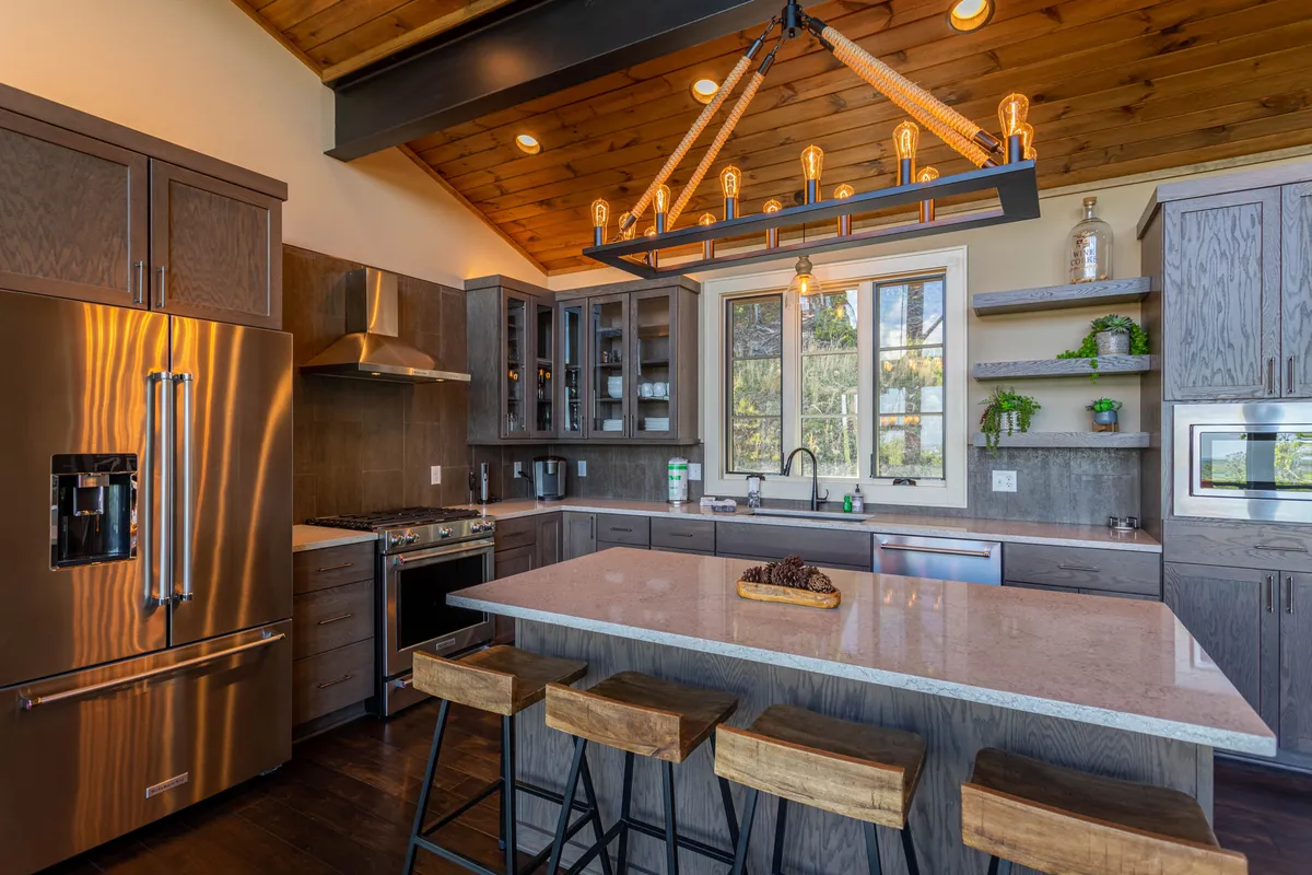 A modern kitchen is highlighted, featuring a central island, stylish chandelier, stainless steel appliances, and pantry shelving. The space feels inviting and functional, ideal for both cooking and casual gatherings.