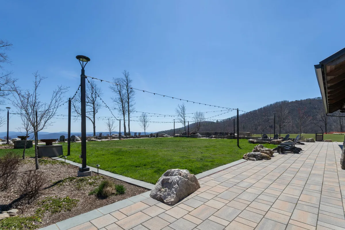 This image features a green lawn with patio seating, string lights, and a mountain view. The expansive outdoor space is inviting for gatherings and playtime, with plenty of room for pets to roam under supervision. The comfortable patio seating areas are ideal for pet-friendly relaxation.