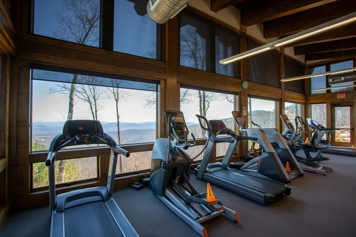 A modern fitness center interior with treadmills positioned before large windows showcasing mountain views. The space is bright and uplifting, encouraging guests to stay active indoors while remaining visually connected to the outdoor environment.