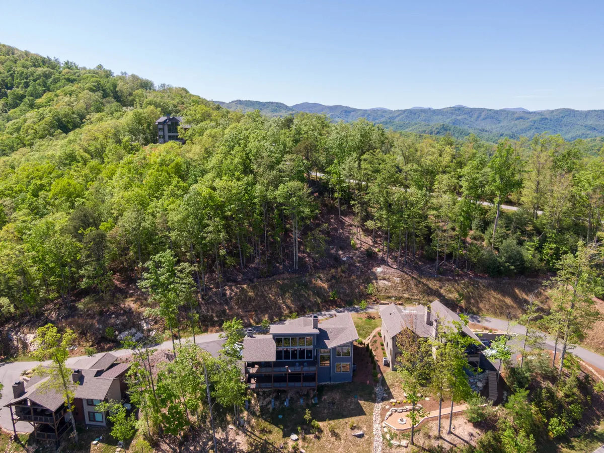 This wide exterior shot shows houses nestled among trees, an expansive mountain view, and a winding road leading into the property. The landscape emphasizes the sense of adventure, access to nature trails, and the secure, community-oriented atmosphere highlighted in the section.
