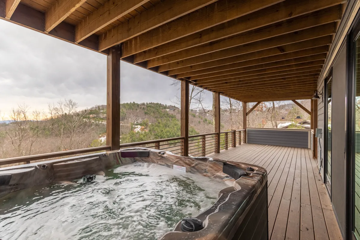 A scenic exterior shot of a wooden deck featuring a modern hot tub overlooking a stunning mountain view. The inviting hot tub is positioned for relaxation, with sweeping vistas that promise tranquil evenings or post-adventure soaks.