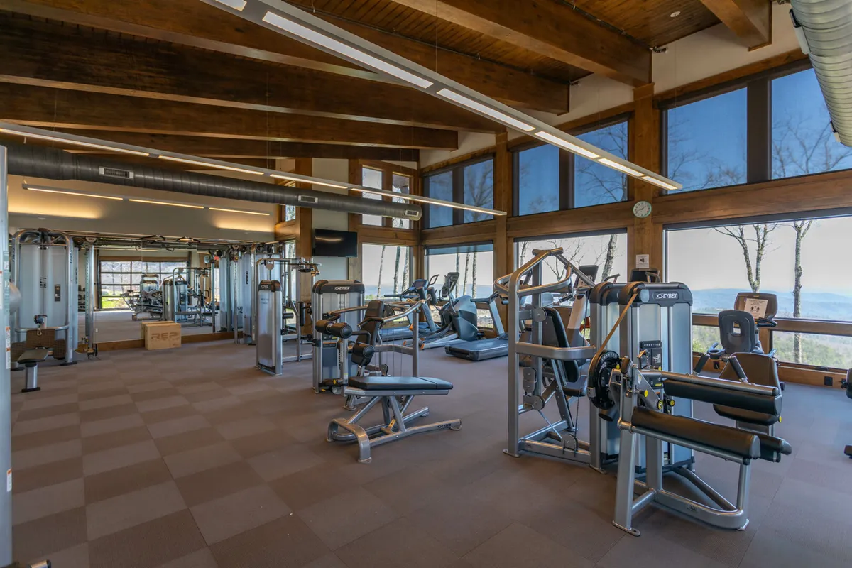 A bright, modern interior fitness center with state-of-the-art exercise equipment and expansive windows that frame stunning views of the surrounding landscape. Guests are working out, energized by the natural light and scenic vistas.