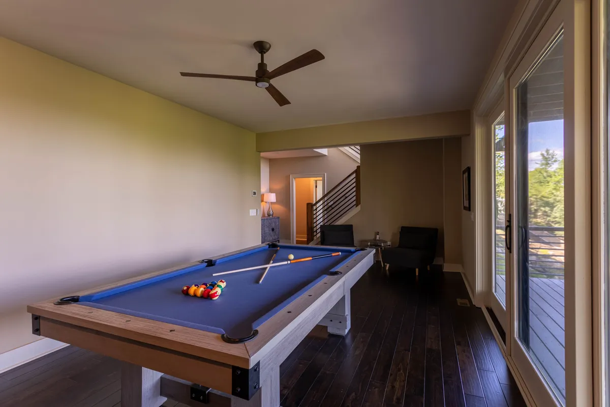 A casual game room scene with a pool table, comfortable seating, and a view through sliding glass doors that hint at easy indoor-outdoor flow. Natural light and a relaxed setup encourage both competition and relaxation.