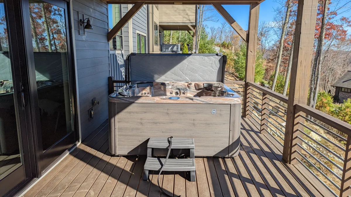 The image features a private outdoor hot tub set on a wooden deck, surrounded by lush trees. The tranquil setting is bathed in natural light, evoking peacefulness and relaxation. This inviting area offers views of the surrounding nature, perfectly suited for unwinding after a day of exploration.